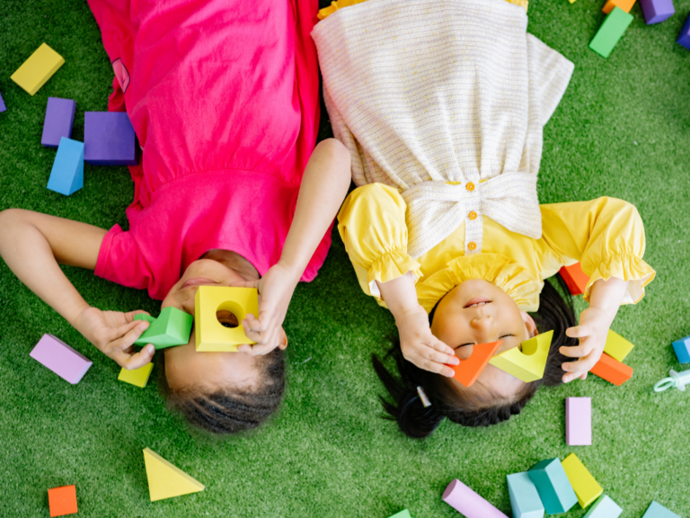 Dzieci leżące na trawie i bawiące się klockami podczas zajęć terapeutycznych